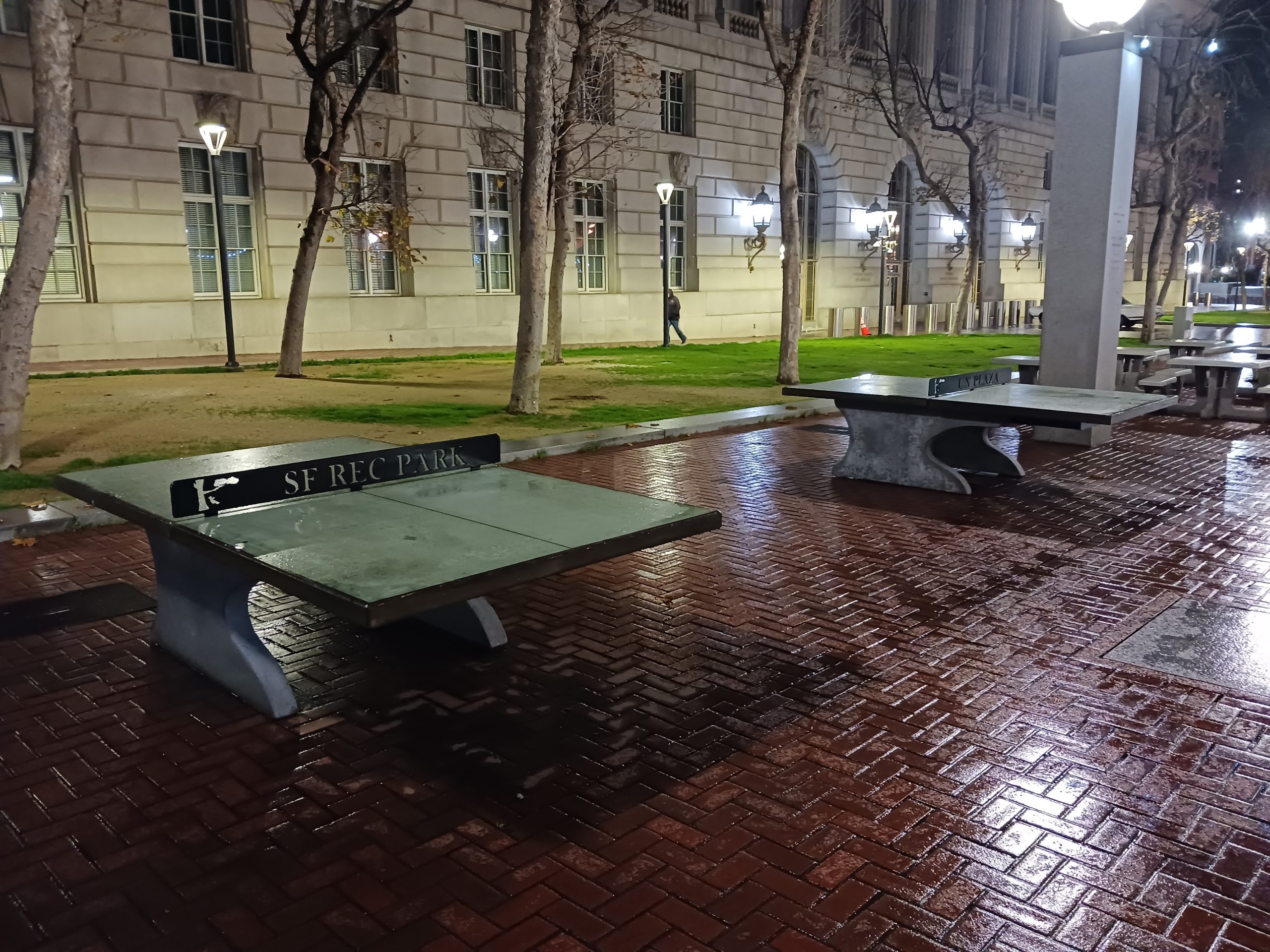 Ping pong tables on a brick walkway at night.