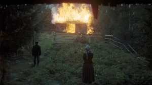 Two people standing in front of a burning cabin.