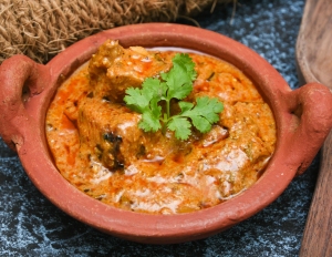 Indian chicken curry in a clay pot on a table.