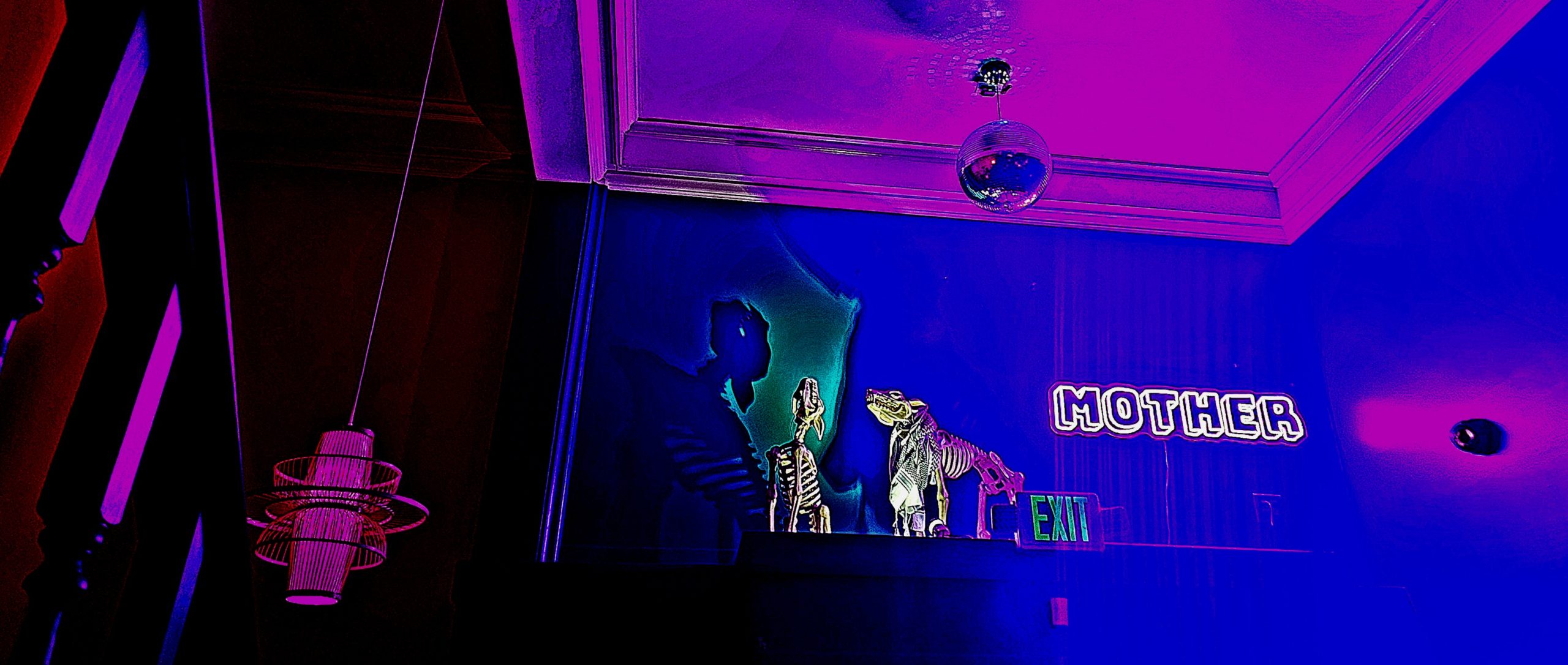 In a room with purple lighting, white neon light sign that says "MOTHER" hangs on the wall.