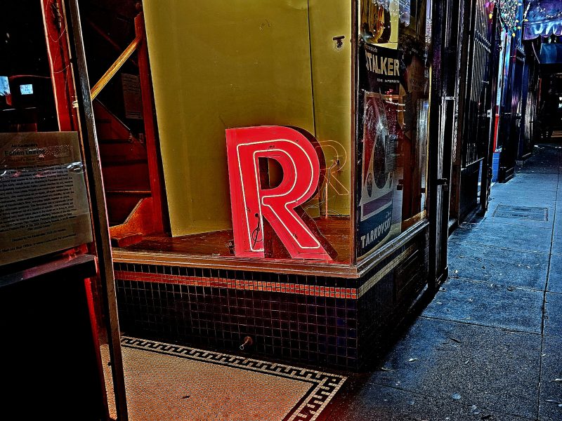A red neon sign of the letter R in the window of a building.