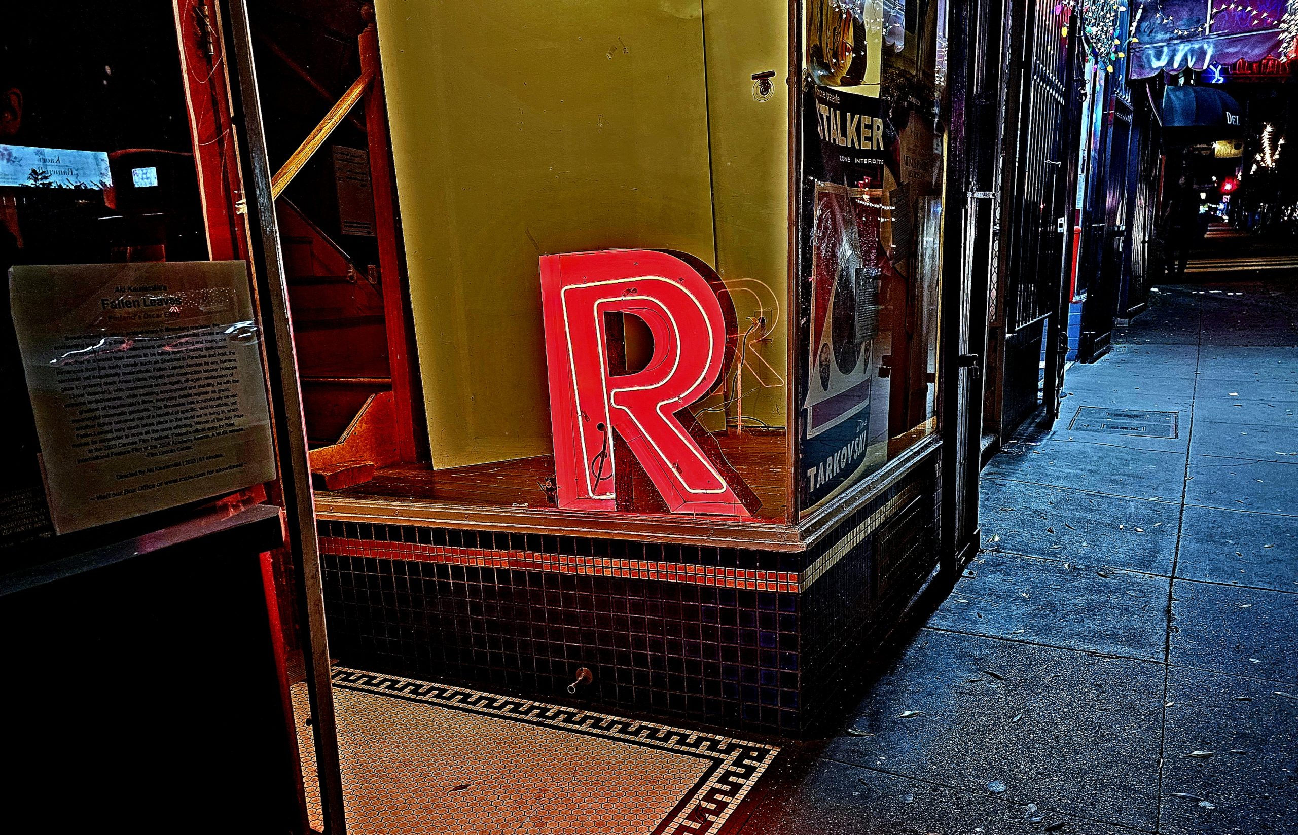 A red neon sign of the letter R in the window of a building.