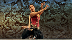 A woman is performing a dance in front of a stone wall.