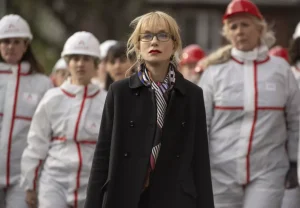 A woman in glasses is standing in front of a group of construction workers.