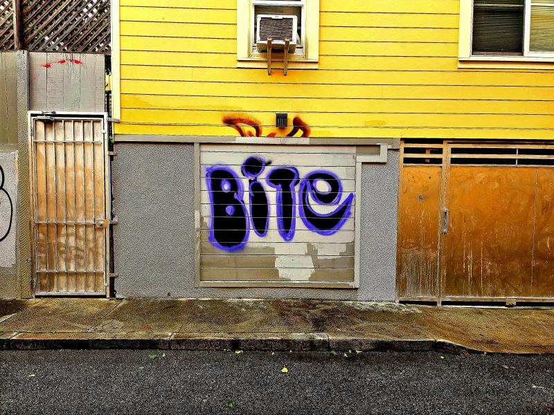 A yellow building with spray paint that says Bite.