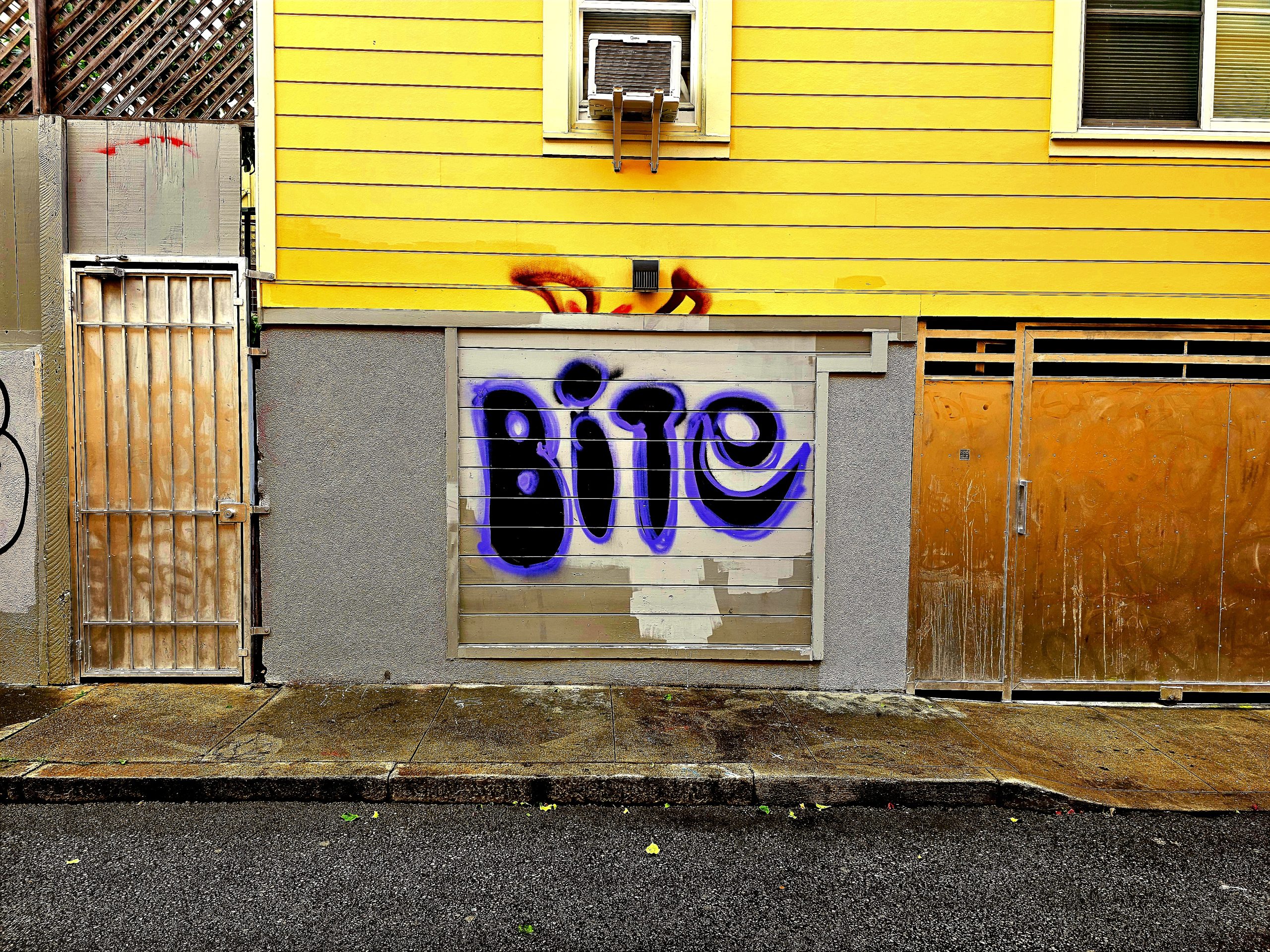 A yellow building with spray paint that says Bite.