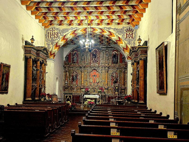 The inside of a church with wooden pews and religious murals on the walls.