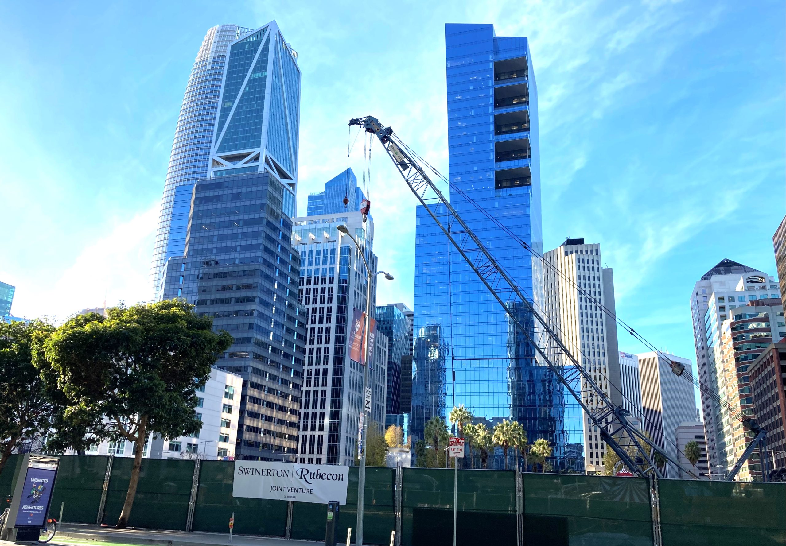 A crane at a construction site in San Francisco. Skyscrapers under the blue sky are in the background.