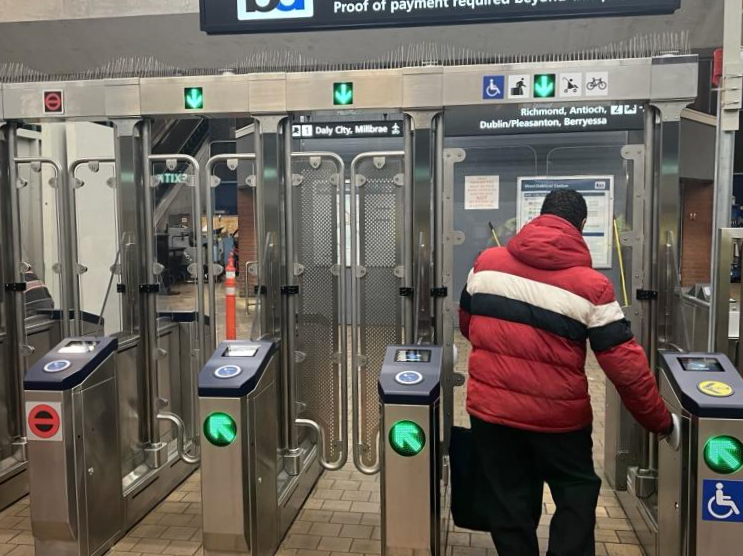 A man passing a fare gate at West Oakland BART station.