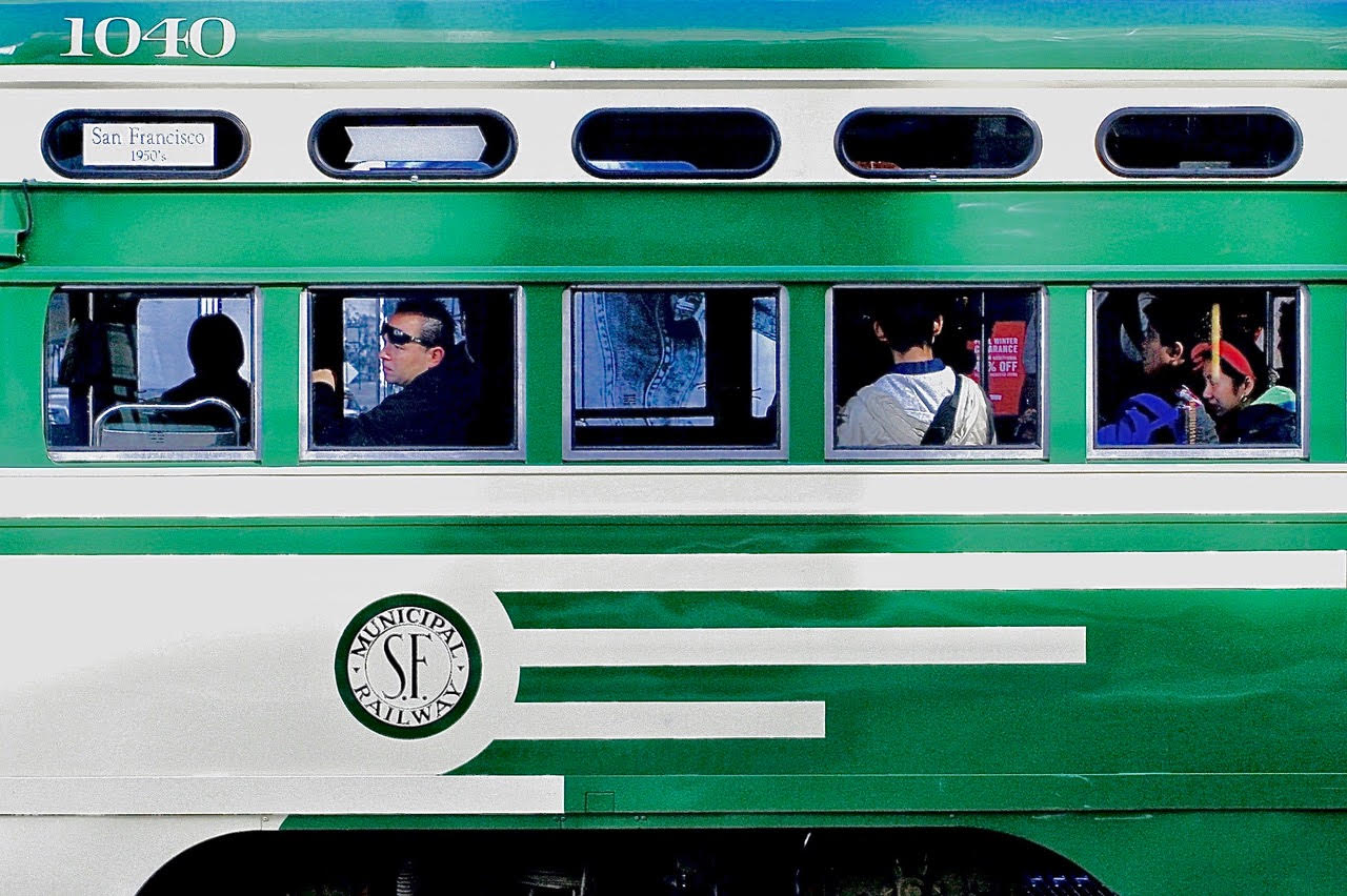A green and white cable car with passengers sitting by the window.