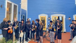 A group of people standing in front of a blue building with saxophones.