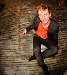 A man in a suit sitting on a wooden floor.