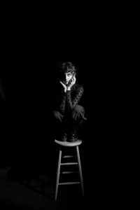 A black and white photo of a woman sitting on a stool.