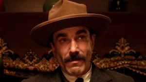 A man in a hat and suit sitting in front of a fireplace.