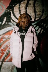 A man with dreadlocks standing in front of a graffiti wall.