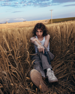 A woman sitting in a wheat field holding a gun.