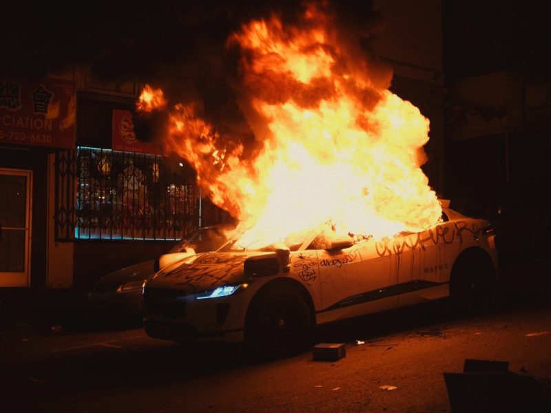 A car is on fire in front of a building.