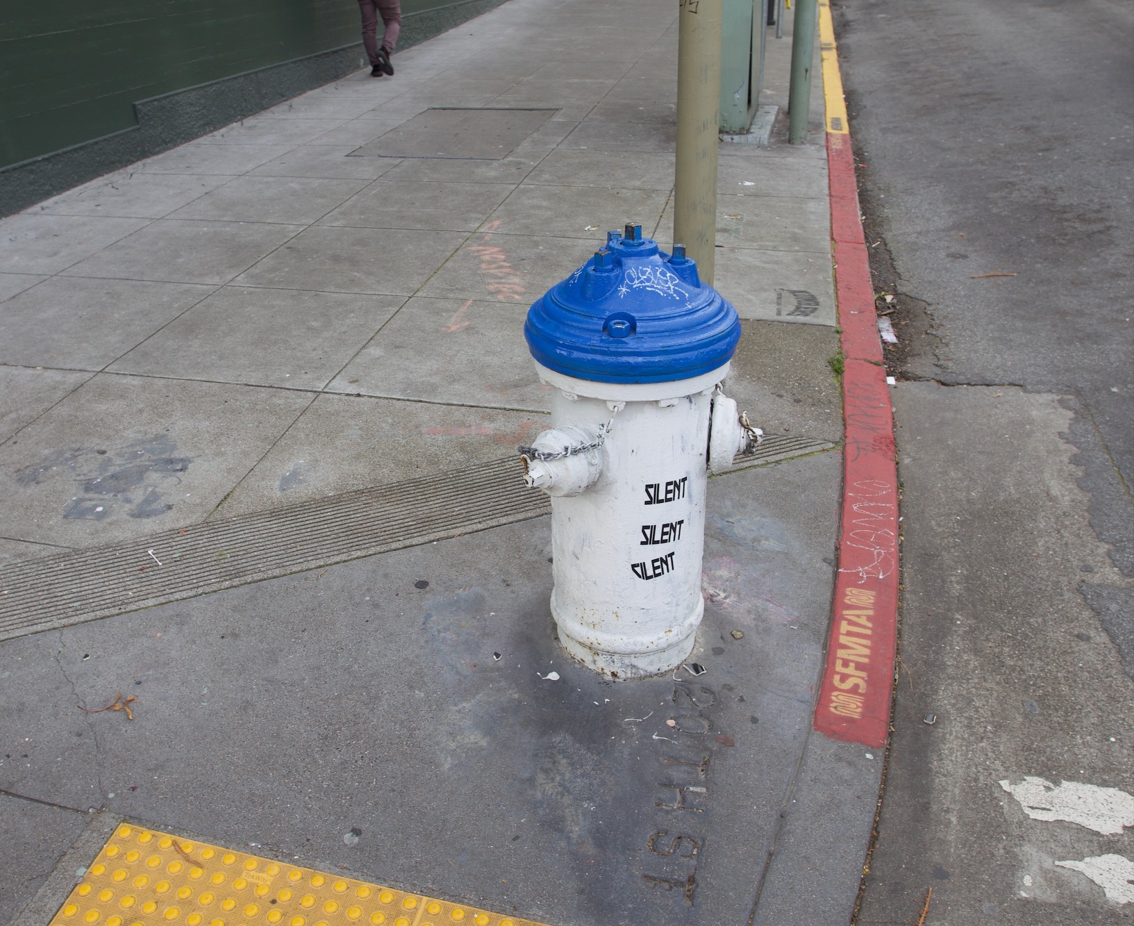 A blue and white fire hydrant on a sidewalk. The word silent is stenciled on to it three times.