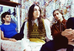 Three people sitting on a bed next to a floral pattern.