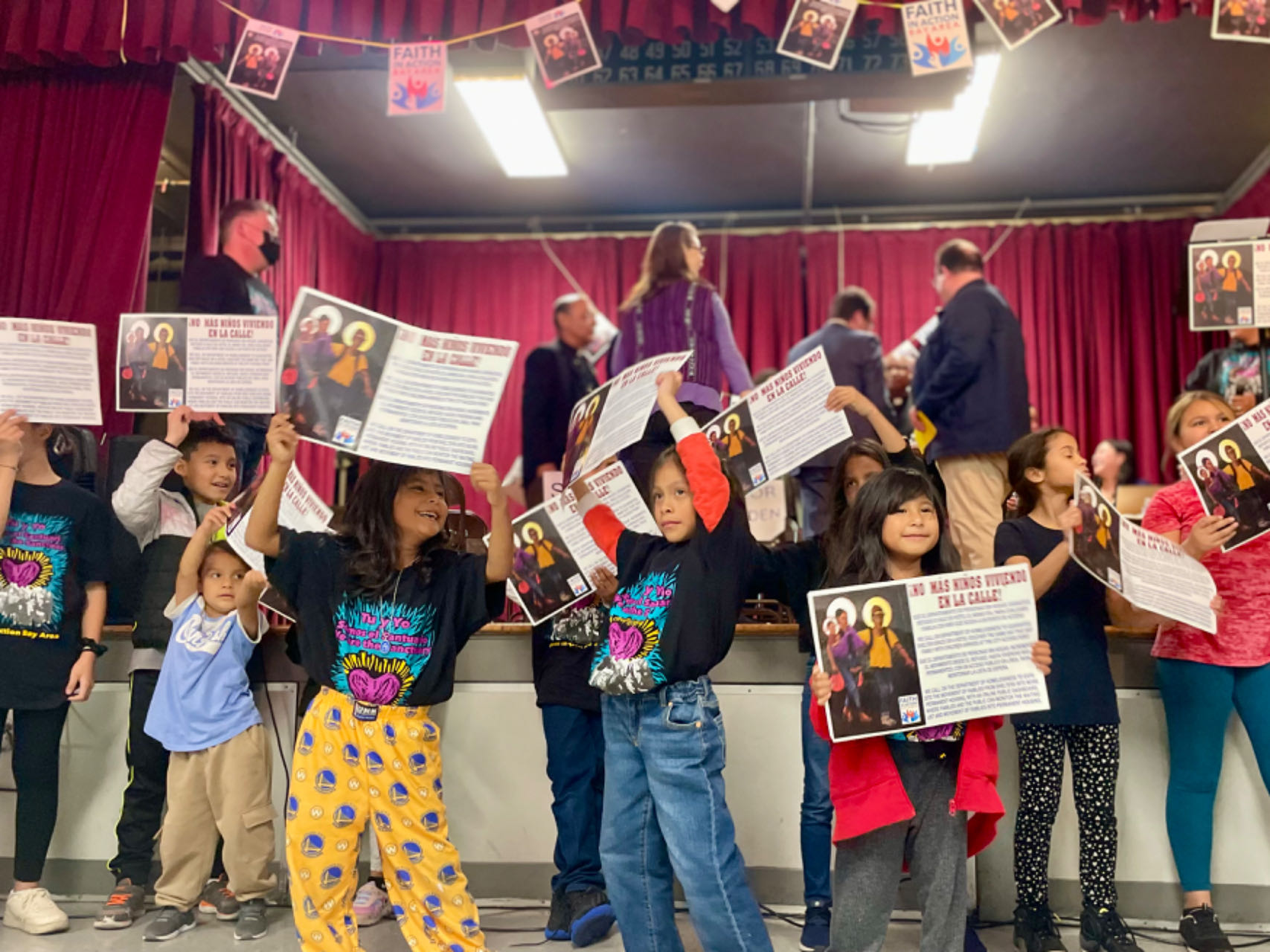 Children on a stage holding up papers with enthusiasm.