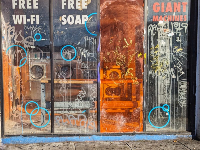 A storefront with graffiti-covered windows advertising "free wi-fi," "free soap," and "giant machines.