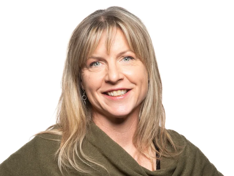 Portrait of a smiling woman with shoulder-length blonde hair and a green shawl.