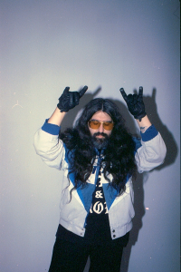 Person in a wig and beard gesturing rock-on signs against a plain background.