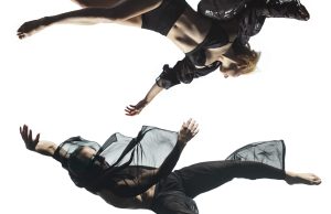 Two dancers in mid-air, performing an acrobatic move against a white background.