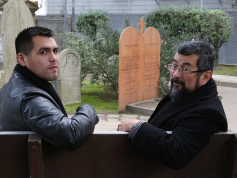 Vincent Medina and Andrew Galvan sit near a memorial for their ancestors, Jobocme and Poylemja, in the Mission Dolores cemetery.