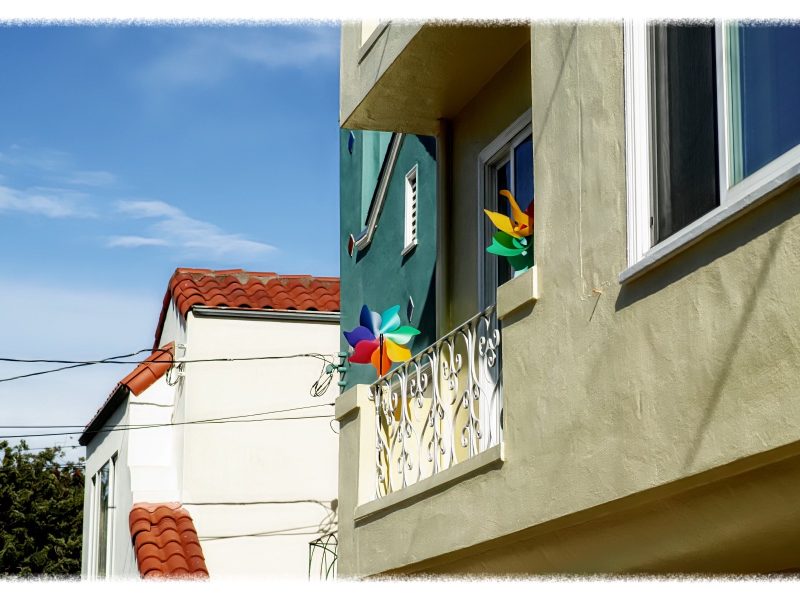 Colorful pinwheel decorations on a sunny balcony with a blue sky background.
