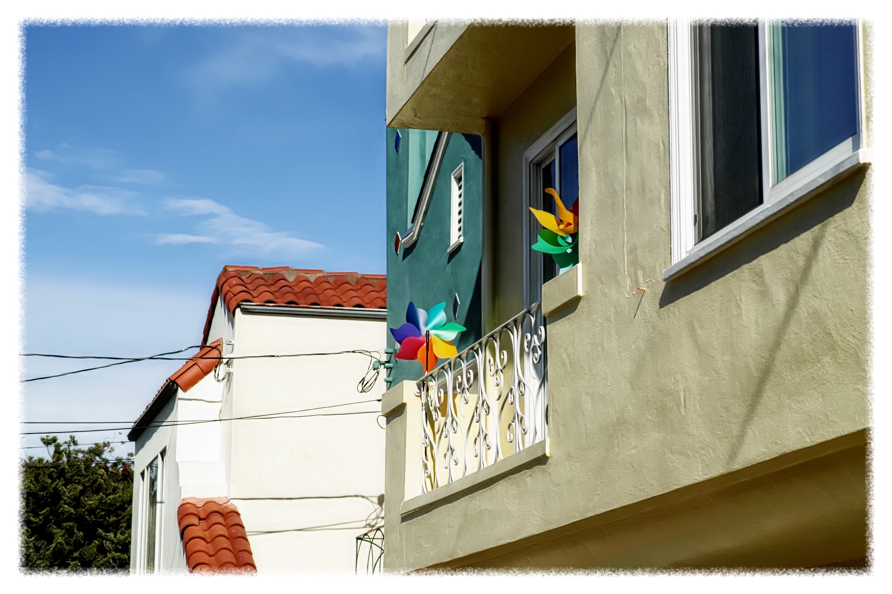 Colorful pinwheel decorations on a sunny balcony with a blue sky background.