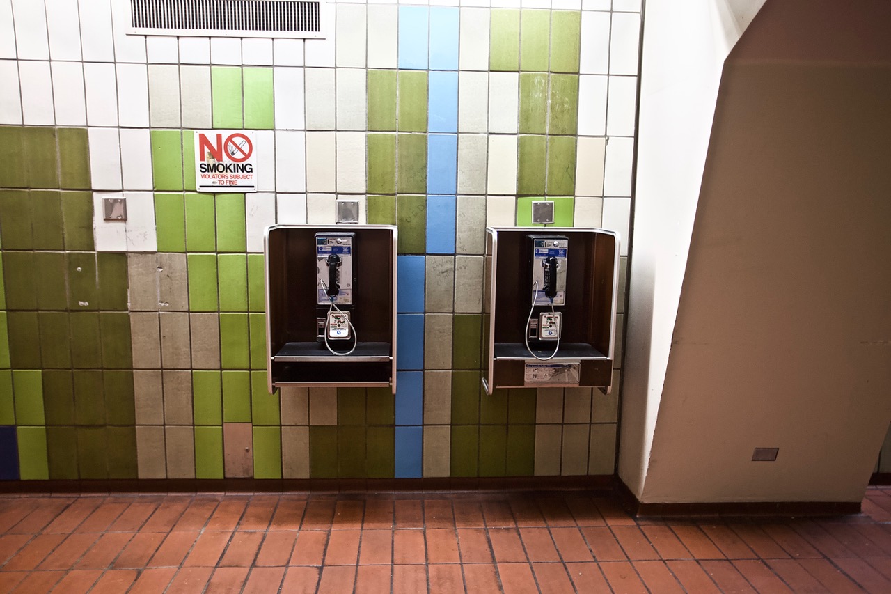 Two payphones mounted on a tiled wall with a 'no smoking' sign above.