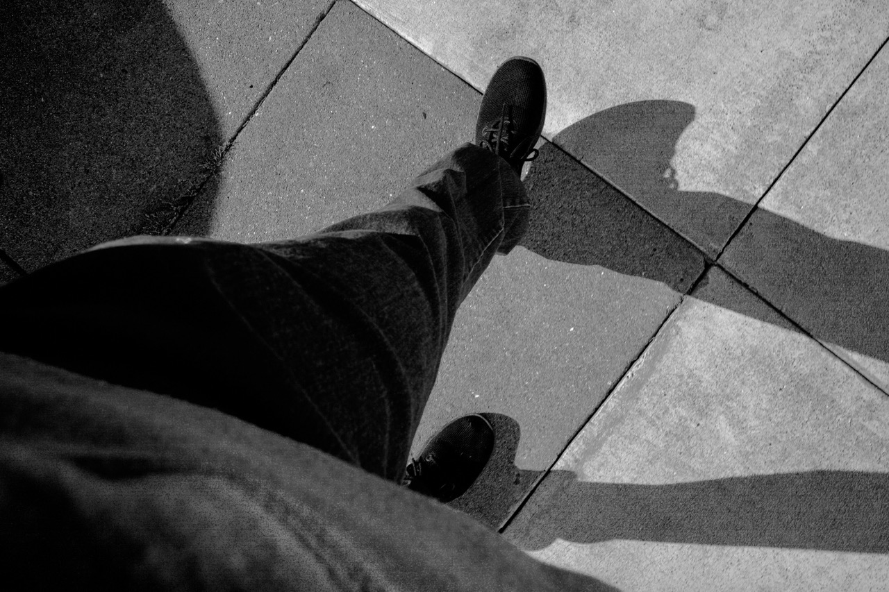 A person's legs and feet on a sidewalk, and their shadow.