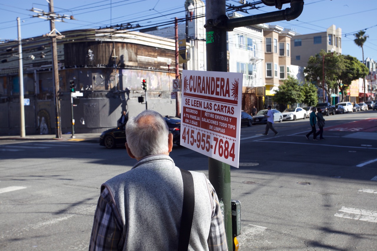 A person observing a street sign advertising curandera services with contact details.