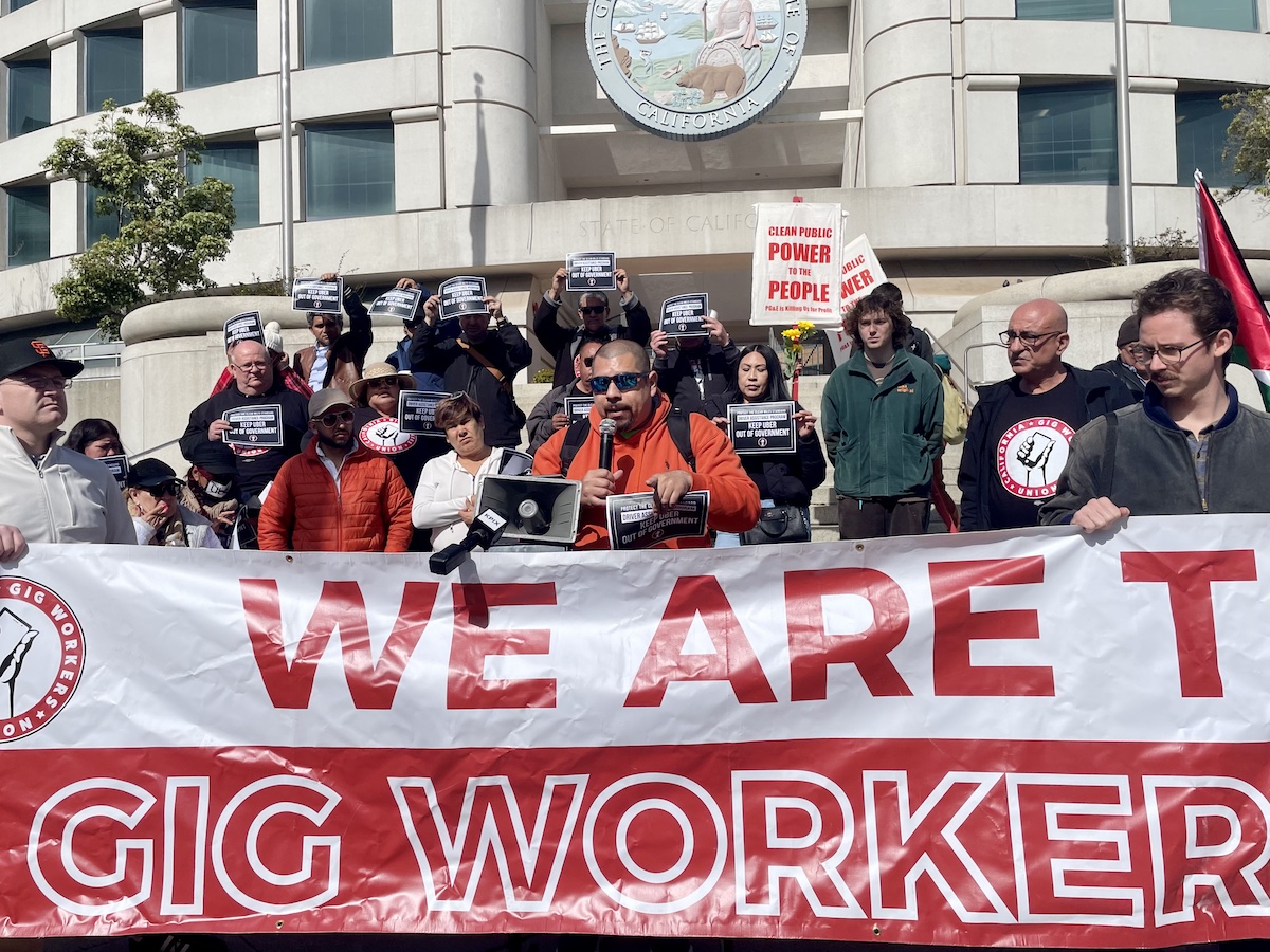 Group of gig workers at a demonstration holding signs and a banner reading "we are gig workers.