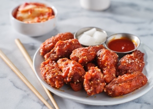 A plate of korean fried chicken with sides of pickled radish, hot sauce, and sugar cubes, accompanied by chopsticks.