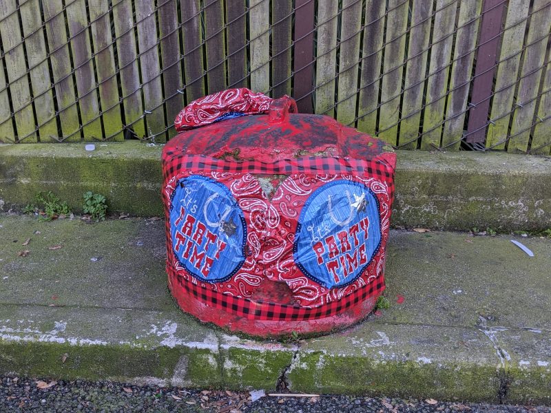Red and blue bandana-covered traffic bollard with party decorations.