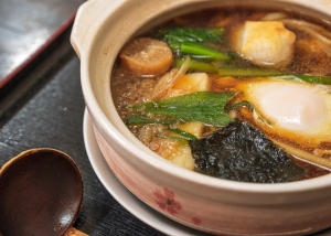 A traditional japanese miso soup with tofu, seaweed, and green onions, served in a ceramic bowl with a wooden spoon.