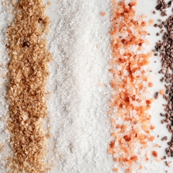 Various types of salt and spices arranged in lines on a surface.
