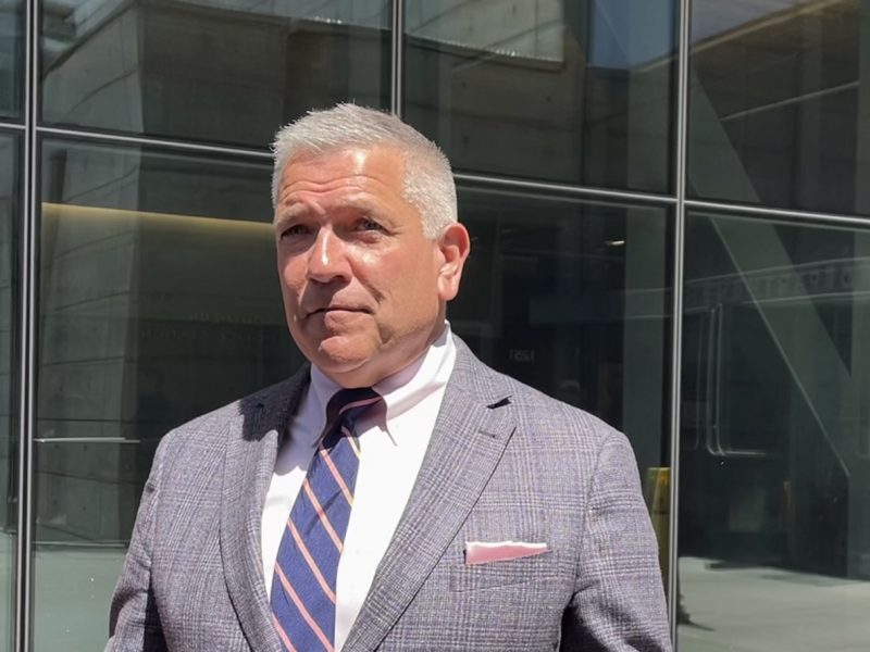Man in a suit with a tie and pocket square standing outside a building with glass facade.