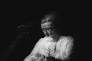 A blurry black and white photo of a person playing guitar and singing into a microphone.