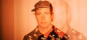 Double exposure portrait of a man in a floral shirt and cap.