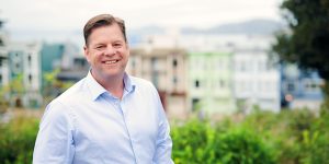 Man smiling outdoors with urban background.