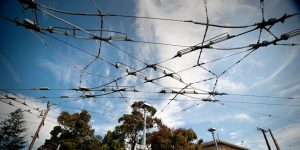 Overhead network of electric tramway cables against a cloudy blue sky.