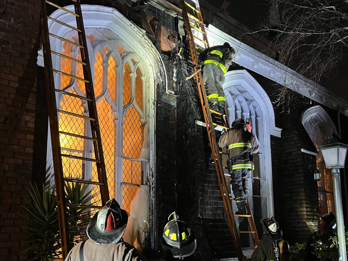 Firefighters working at night on ladders against a building with illuminated windows.