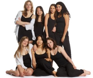 A diverse group of smiling young women posing in black attire against a white background.