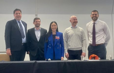 Five professionals, four men and one woman, smiling and standing together behind a conference table in a meeting room.
