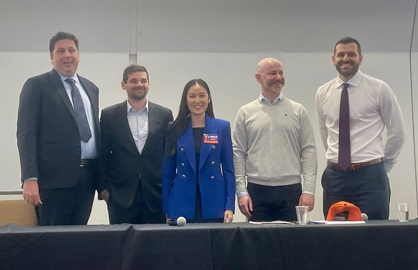 Five professionals, four men and one woman, smiling and standing together behind a conference table in a meeting room.