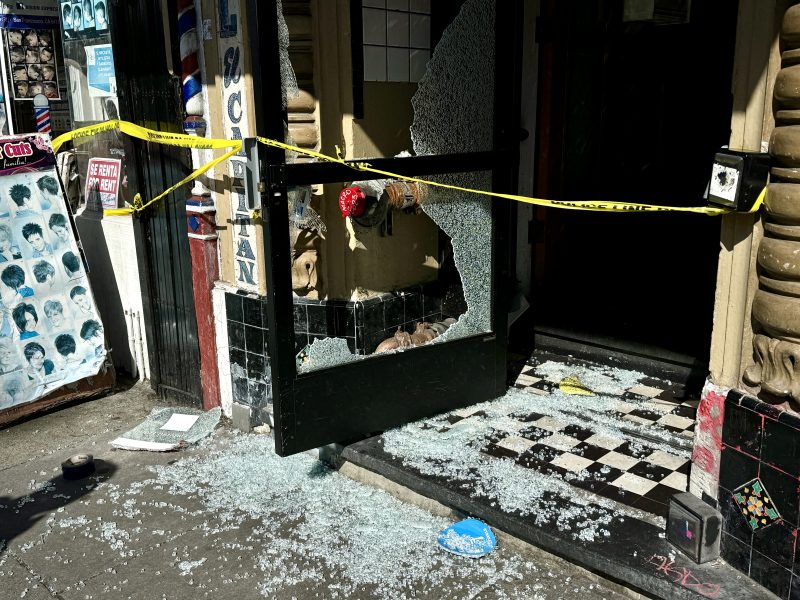 Broken storefront window with caution tape and scattered glass on the sidewalk.