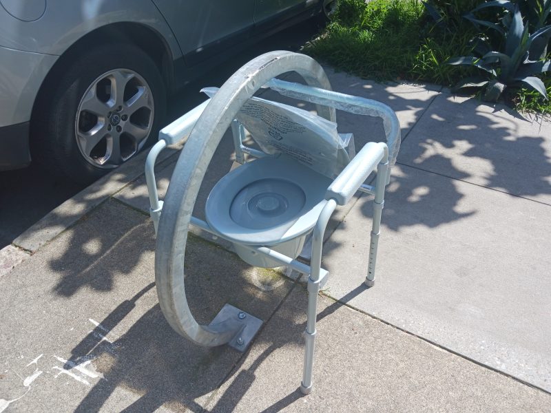 A mobile white plastic toilet stuck in a round metal bike rack.